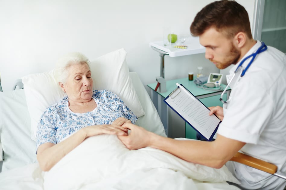 Nurse checks her patients hand in senior living facility bed